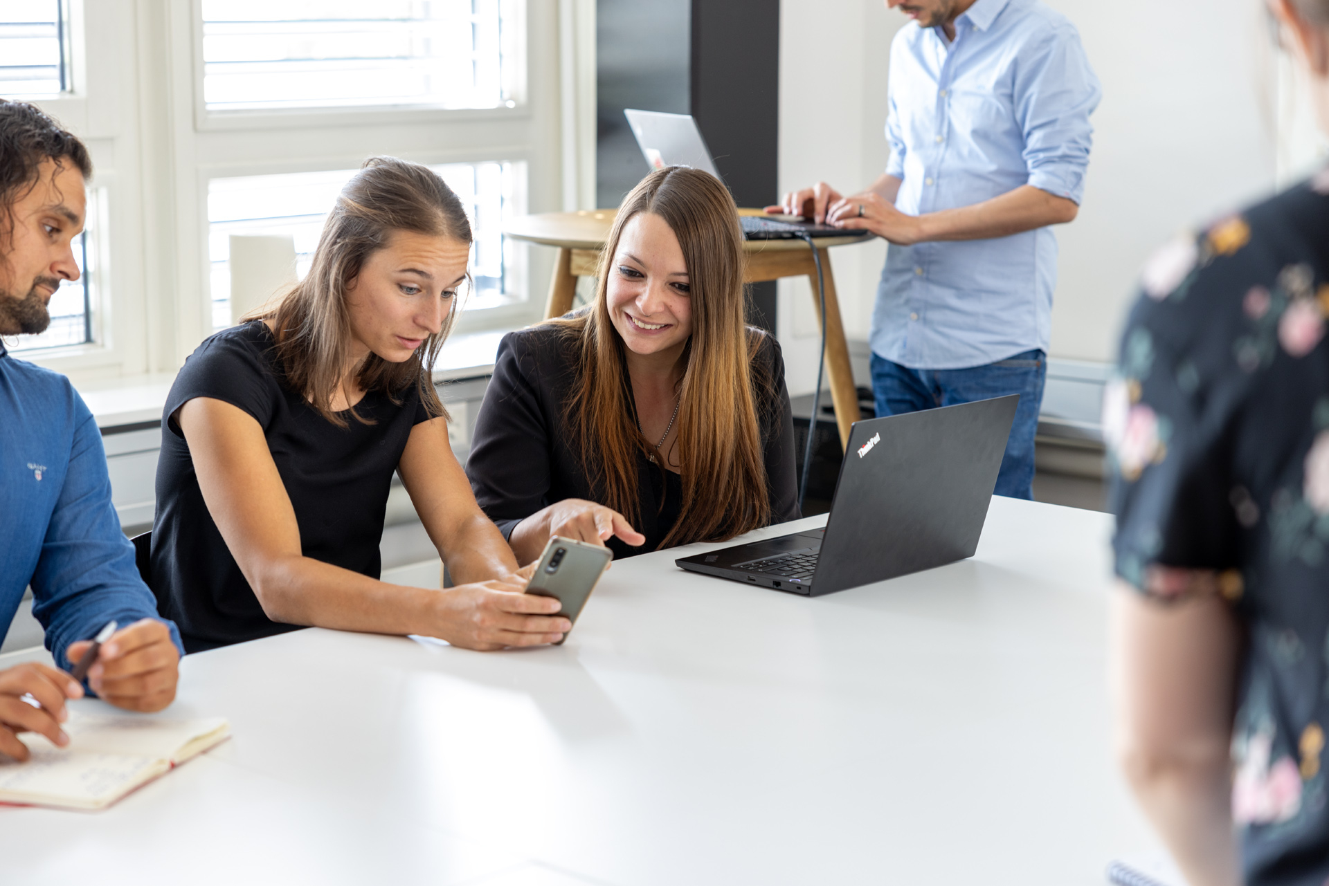 Mitarbeitende der iqual sitzen am Tisch und schauen sich etwas am Smartphone und am Laptop an