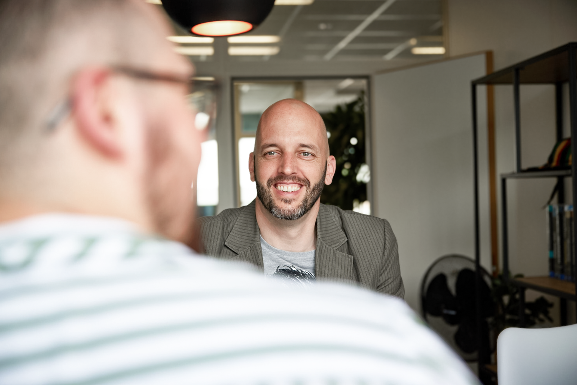 iqual Mitarbeiter sitzt an Tisch und lacht in die Kamera